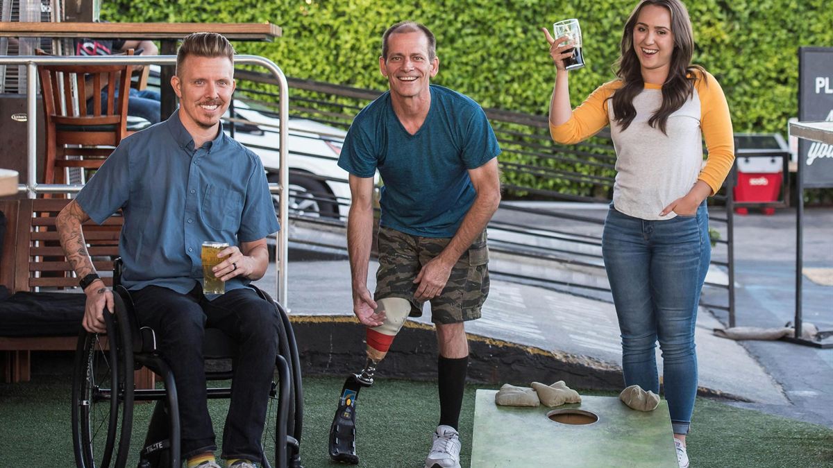 Three friends, including a wheelchair user and an amputee, laughing over a lawn game